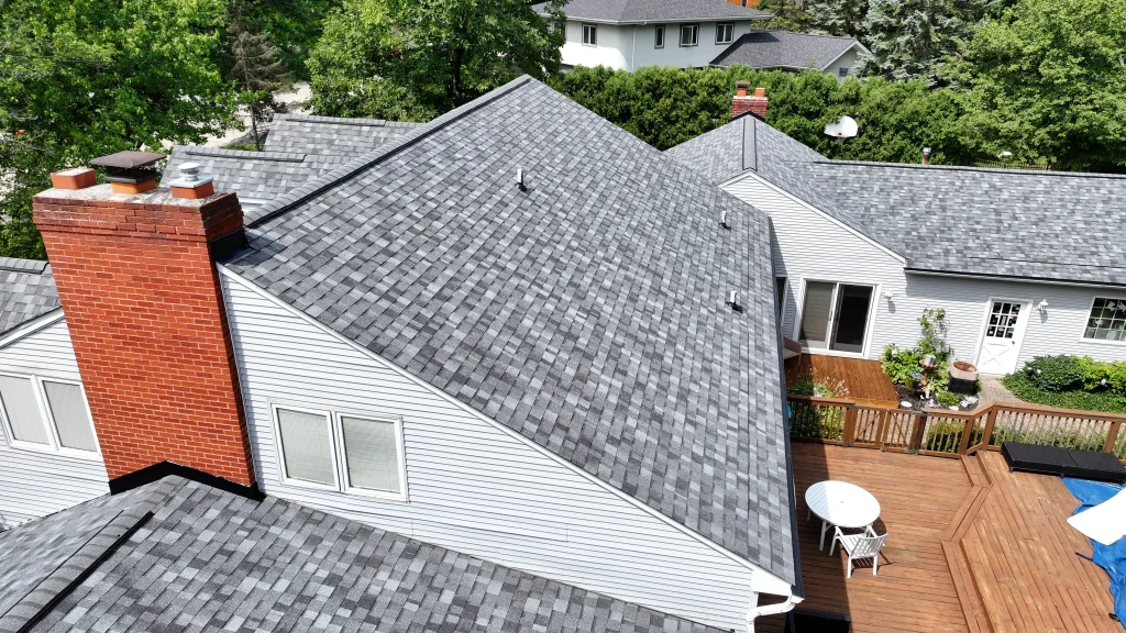 Aerial view of new gray asphalt shingles installed around a brick chimney